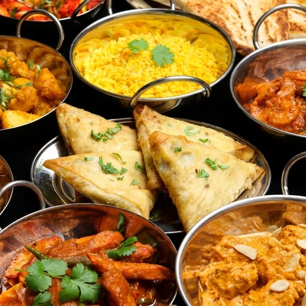 A variety of Indian dishes, including curries, rice, samosas, and naan bread, in metal bowls.