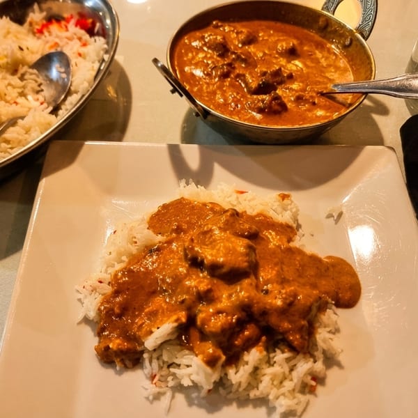 Indian butter chicken curry and basmati rice served on a white plate and in metal bowls.