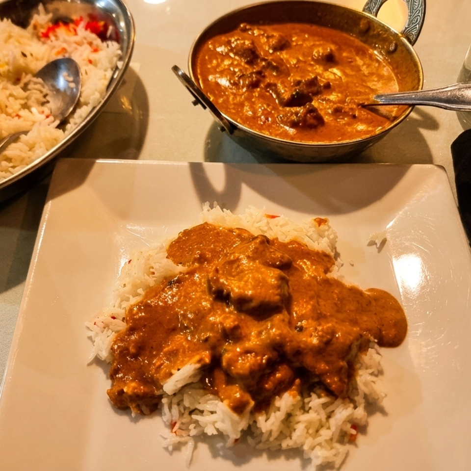 Indian butter chicken curry and basmati rice served on a white plate and in metal bowls.