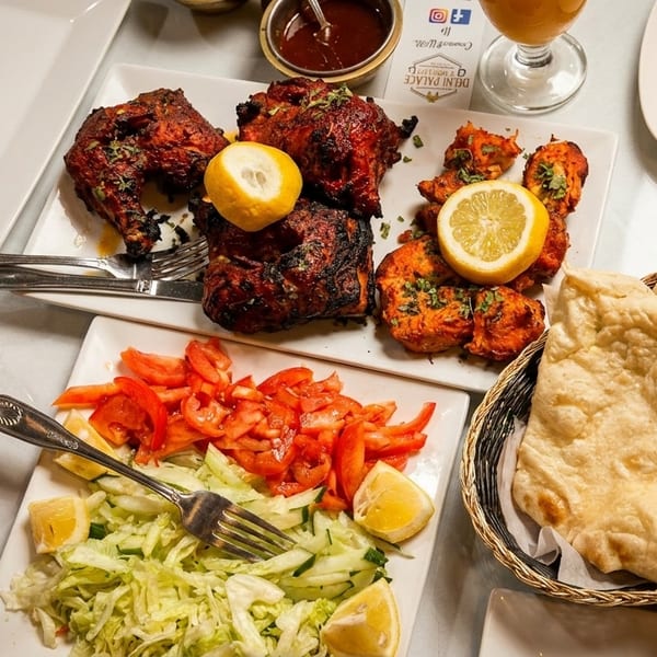 A table laden with Indian dishes including tandoori chicken, curry, naan, and salad.